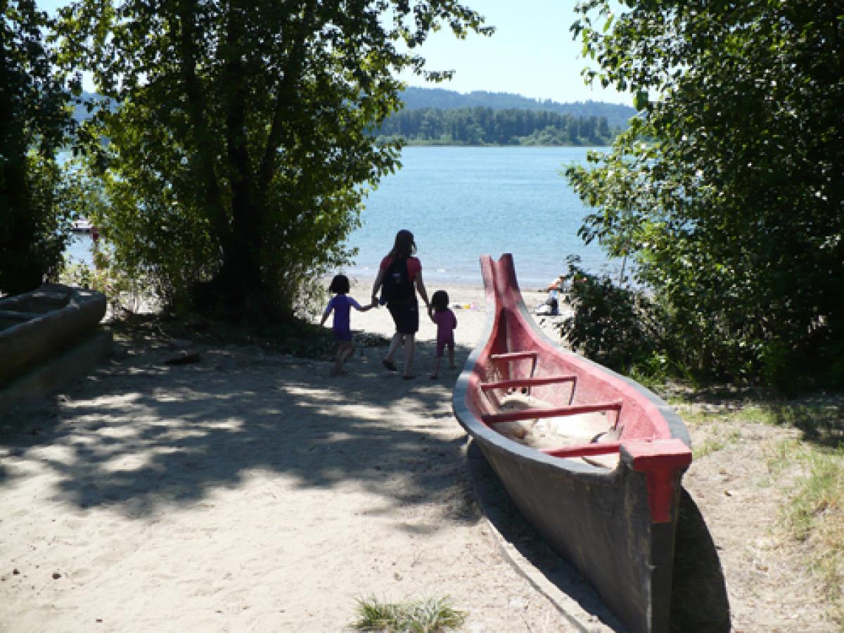 Woman with two kids walking toward the beach, models of canoes in the foreground